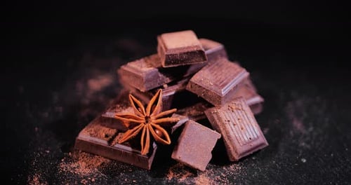 Fundo giratório de pedaços de chocolate com estrelas de anis e cacau em pó. Pedaços de Sweet Dark