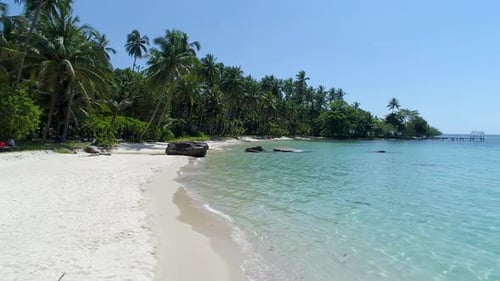 Aerial, drone shot over the shallow, turquoise sea, palm trees and a paradise beach, on a sunny day,