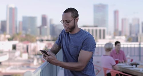 Man Uses Phone on City Rooftop Terrace