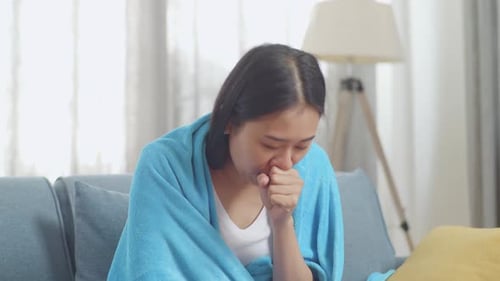 Gros plan d'une femme asiatique malade avec une couverture souffrant de toux sur le canapé dans le salon à la maison