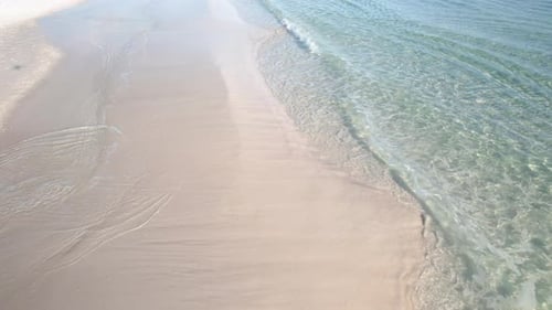 Aerial view of a white sand beach with emerald water waves on a beach