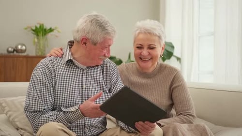 Senior Couple Relaxing and Laughing with Tablet at Home