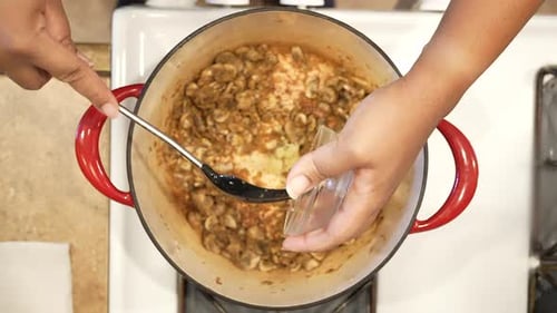 Adding organic minced garlic to mushrooms sauteing on the stove and stirring them in - overhead view
