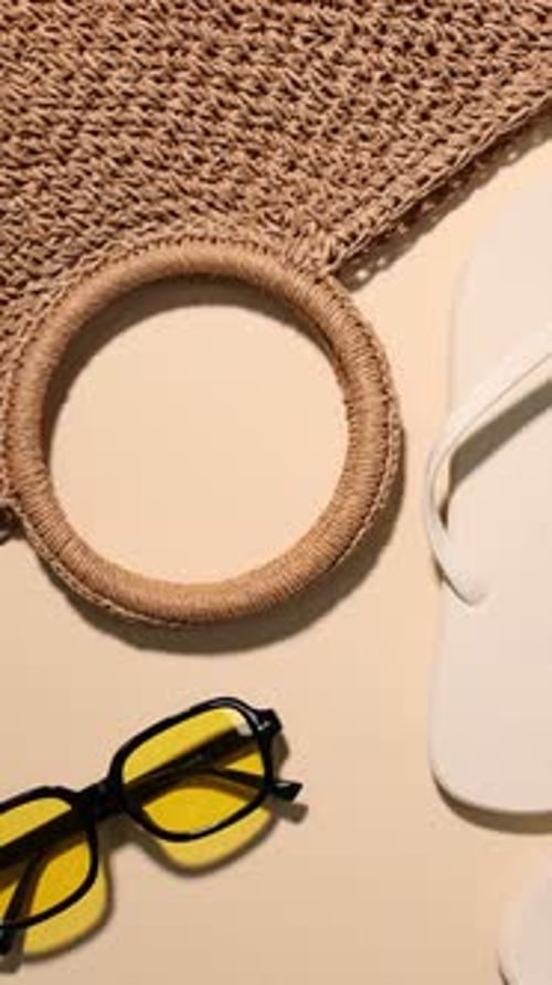 Elegantes chanclas, bolso, gafas de sol y hojas sobre fondo beige, de forma plana. La cámara se mueve a la derecha