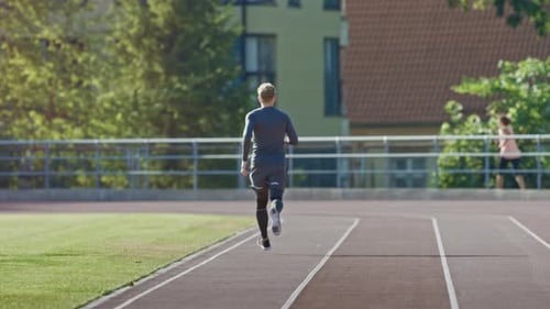 Smiling Athletic Fit Man in Grey Shirt and Shorts Jogging in the Stadium. He is Running Fast on a W