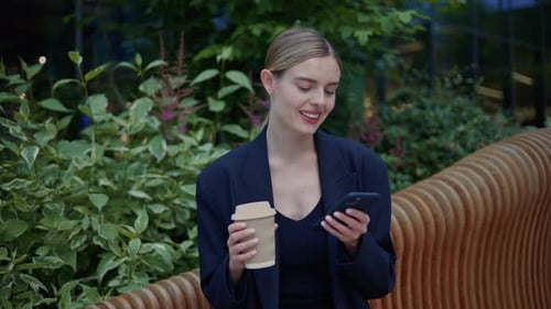 Woman Using Phone, Relaxing in Urban Park with Coffee