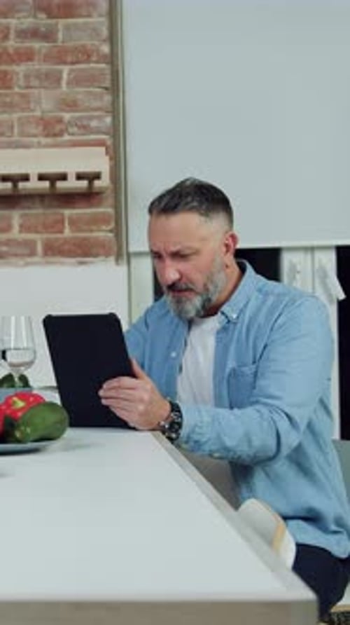 Man Uses Tablet Device at Kitchen Counter Indoors
