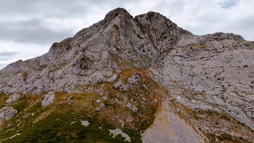 Approaching grey bare high rocks. Low angle view. Rainy cloudscape behind the mountain.