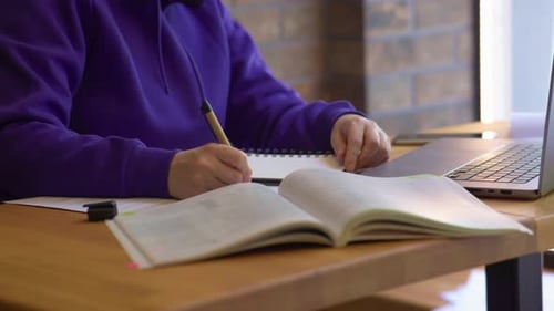 Student Writes in Notebook While Using Laptop