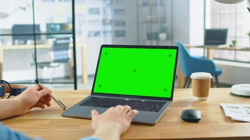 Point of View Shot: Man Uses Laptop Computer with Green Mock-up Screen while Sitting at His Desk. H