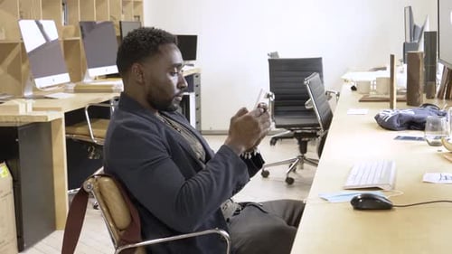 Cheerful millennial entrepreneur texting on phone in startup workspace Canada