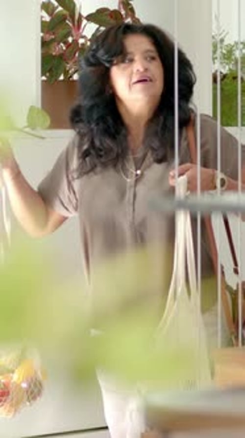 Vídeo vertical: Entrando en casa, una mujer con una blusa de color topo con una bolsa de malla y un bolso que trae comida