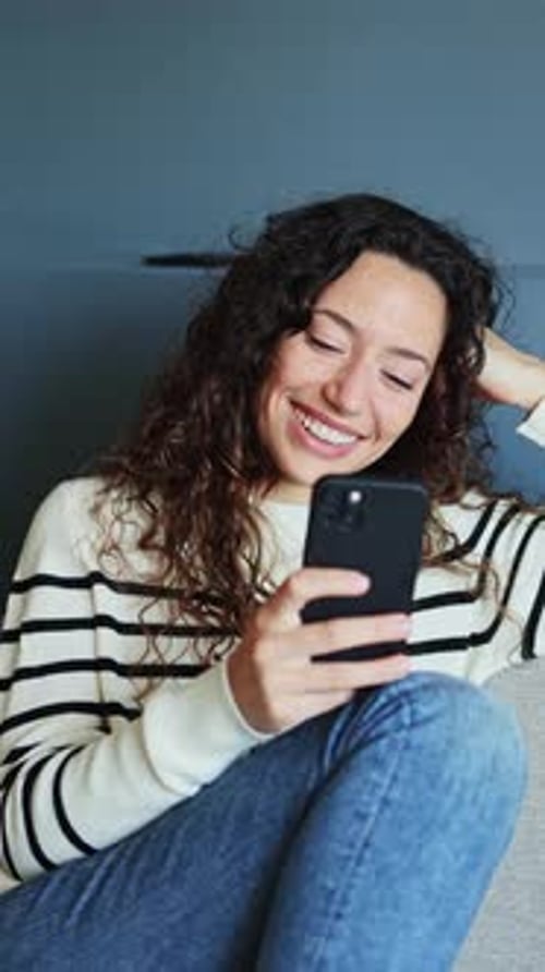 Young Woman Smiles While Using Phone at Home