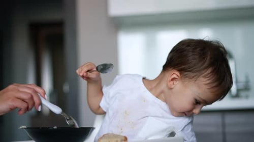 A
mão da mãe dá uma colher cheia para um filho pequeno. O menino ignora a comida e vira a cabeça para o outro lado
.