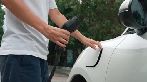 Fortschrittlicher Mann installiert Kabelstecker an die Ladestation seines Elektrofahrzeugs von zu Hause
