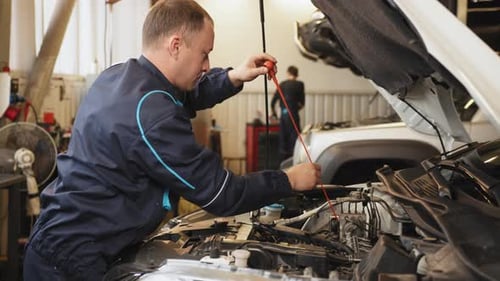 Seitenansicht eines Mechanikers, der das Motoröl in einem Auto mit offener Motorhaube prüft