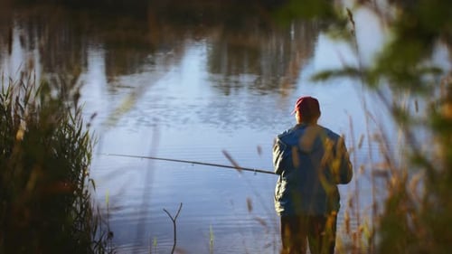 Hombre sereno disfrutando de la experiencia de pesca a primera hora de la mañana junto al tranquilo lago al amanecer rodeado de