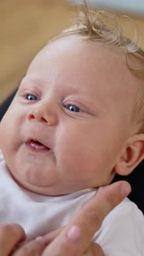Parents play with their adorable baby. Dad's fingers touch cute plump kid's cheeks. Close up.