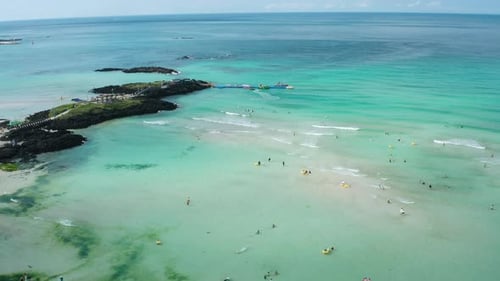 People enjoying swimming and leisure activities at the beach. Drone view of Hamdeok Beach, Jeju Isla