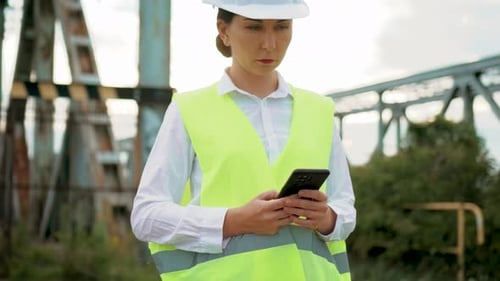 Woman with Hard Hat Looks at Mobile Phone