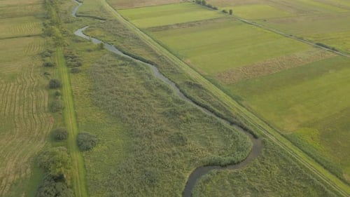 Aerial view of agriculture fields and flowing stream during beautiful summer day.