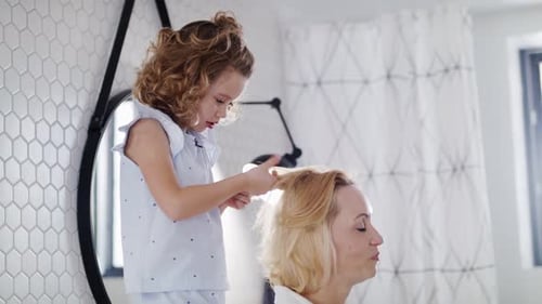 Cute Girl Styling Woman's Hair Indoors in the Home