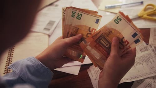 Close Up of Hands Counting Euros While Sitting at a Table Utility Bills and Receipts are on the