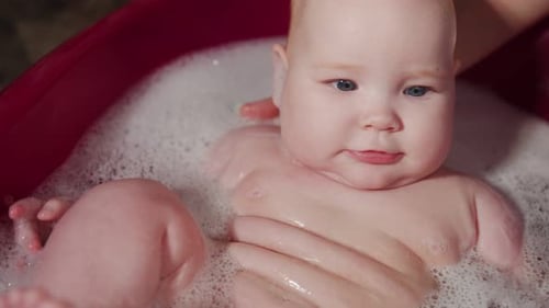 Infant Bathed by Adult in Bubbly Red Tub