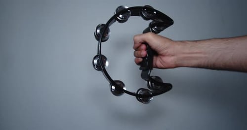 Artist's hand holding and performing with a black tambourine inside a room with white walls. 4K