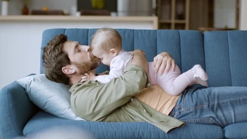 Bearded man lying on couch with his baby