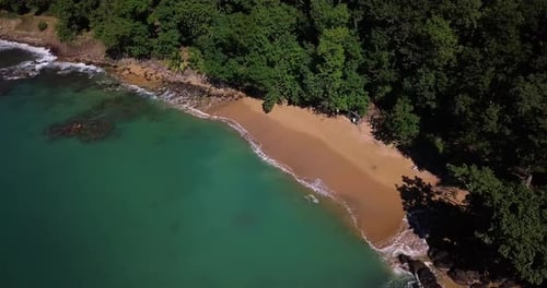Aerial view of a small secluded beach in a cove. Green, lush mountain behind.