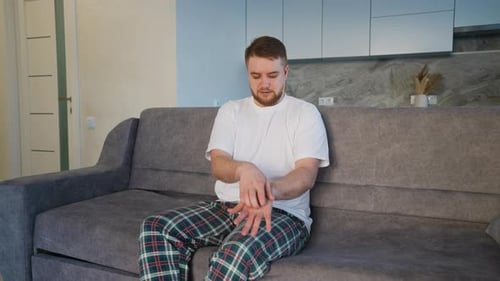 Man on Couch in Pajamas Itching Arm