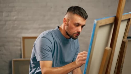 Young Artist in a Blue Tshirt in an Art Studio Working on Painting While Sitting