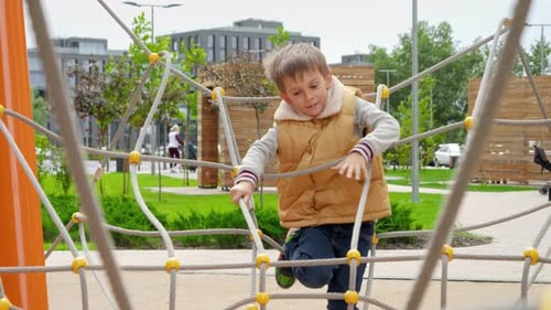 Little boy climbing through obstacles of ropes and nets on new public playground