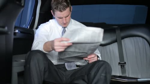 Young man in limousine reading newspaper indoors