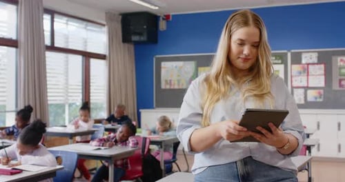 In school, female teacher smiling while students writing at their desks in classroom