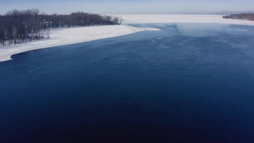 Drone flying over a river near a forest in winter