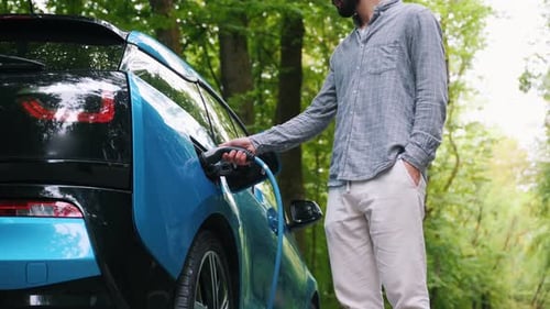 Young man charging electric car outdoor at green forest. Save ecology alternative energy sustainable