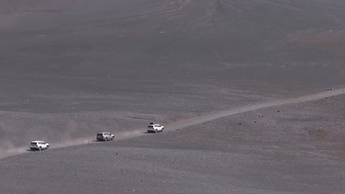 Vehicles Driving on a Winding Dirt Road in Iceland's Volcanic Terrain