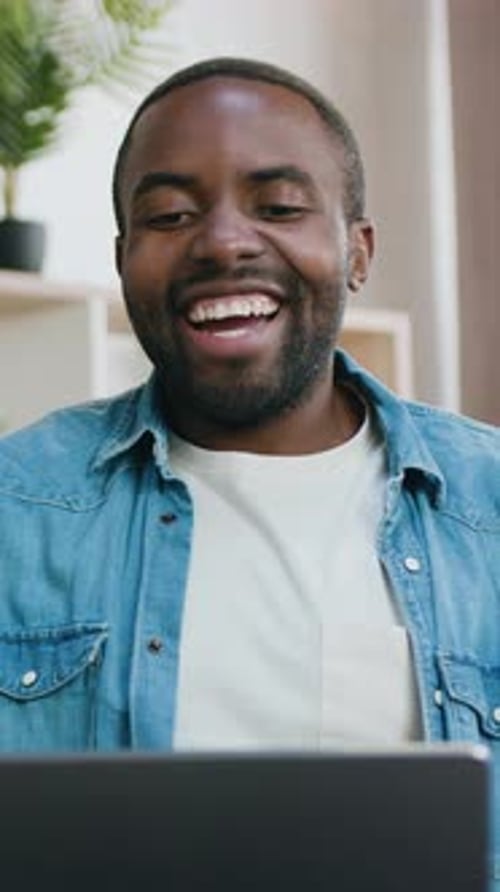 Excited man video conferencing using a laptop indoors