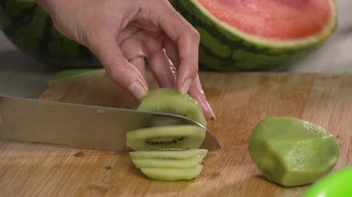 Hands of young woman european slices kiwi fruit with kitchen knife on cutting board