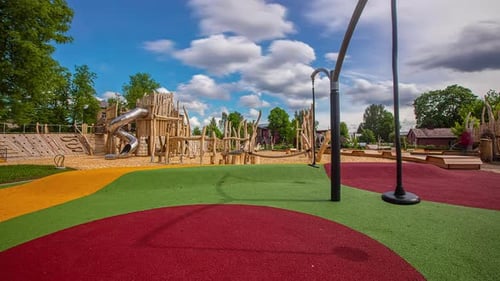 Statische Aufnahme eines bunten Spielplatzbodens zusammen mit Spielgeräten aus Holz auf einem Spielplatz im Freien