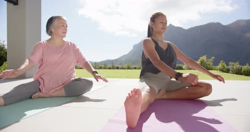 Practicing yoga, women stretching on mats outdoors with mountain view