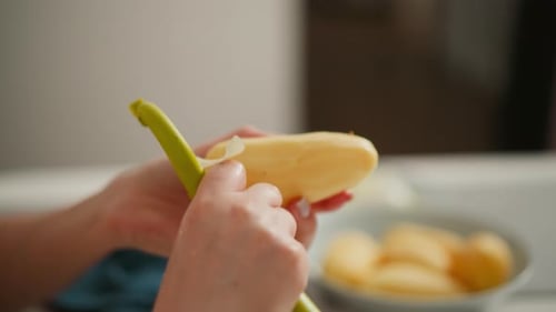 Close Up of Woman Peeling Potato with Blurred Background and Plate of Potatoes
