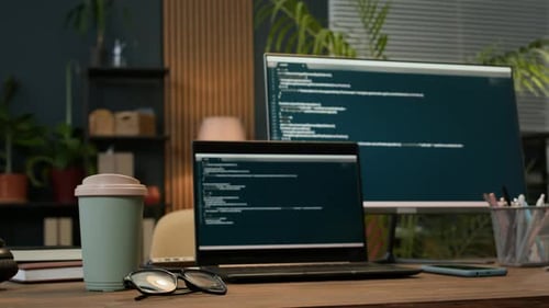 Two Coding Screens on Laptop and Computer at Desk in Modern Office