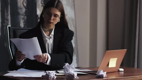 Gestresste Geschäftsfrau sitzt am Schreibtisch mit Laptop und zerknitterten Papieren fühlt sich müde zerknittertes Papier und