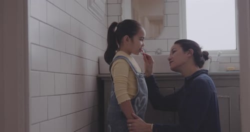 Mother Brushing Daughter's Teeth in Bathroom