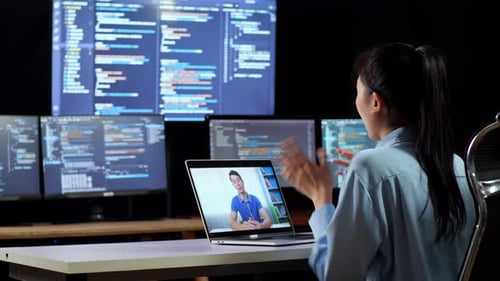 Asian Female Programmer Having A Meeting By A Laptop While Writing Code On Multiple Monitors