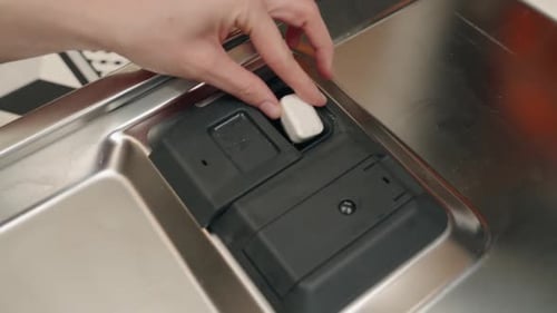 Loading dishwasher with cleaning cube in kitchen