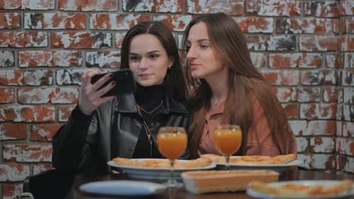 Two Girls are Sitting in a Cafe and Taking a Selfie on the Phone